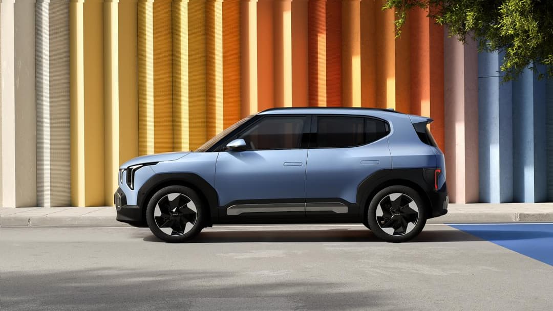 Kia EV2 bleu ciel de profil, compact B-SUV électrique aux lignes modernes, présenté devant un mur aux teintes orange et jaune