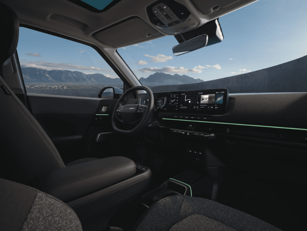 Intérieur du Kia EV2 avec cockpit numérique, écrans de 12,3 pouces et accents verts, vue montagne par le pare-brise
