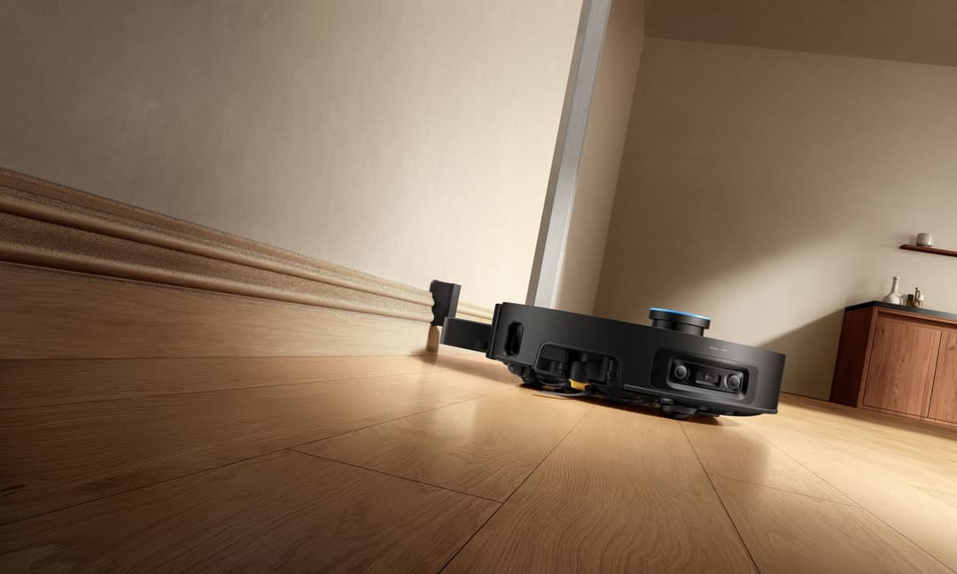 Robot aspirateur Dreame X60 Pro noir équipé d'un bras articulé sur parquet, près d'une plinthe blanche
