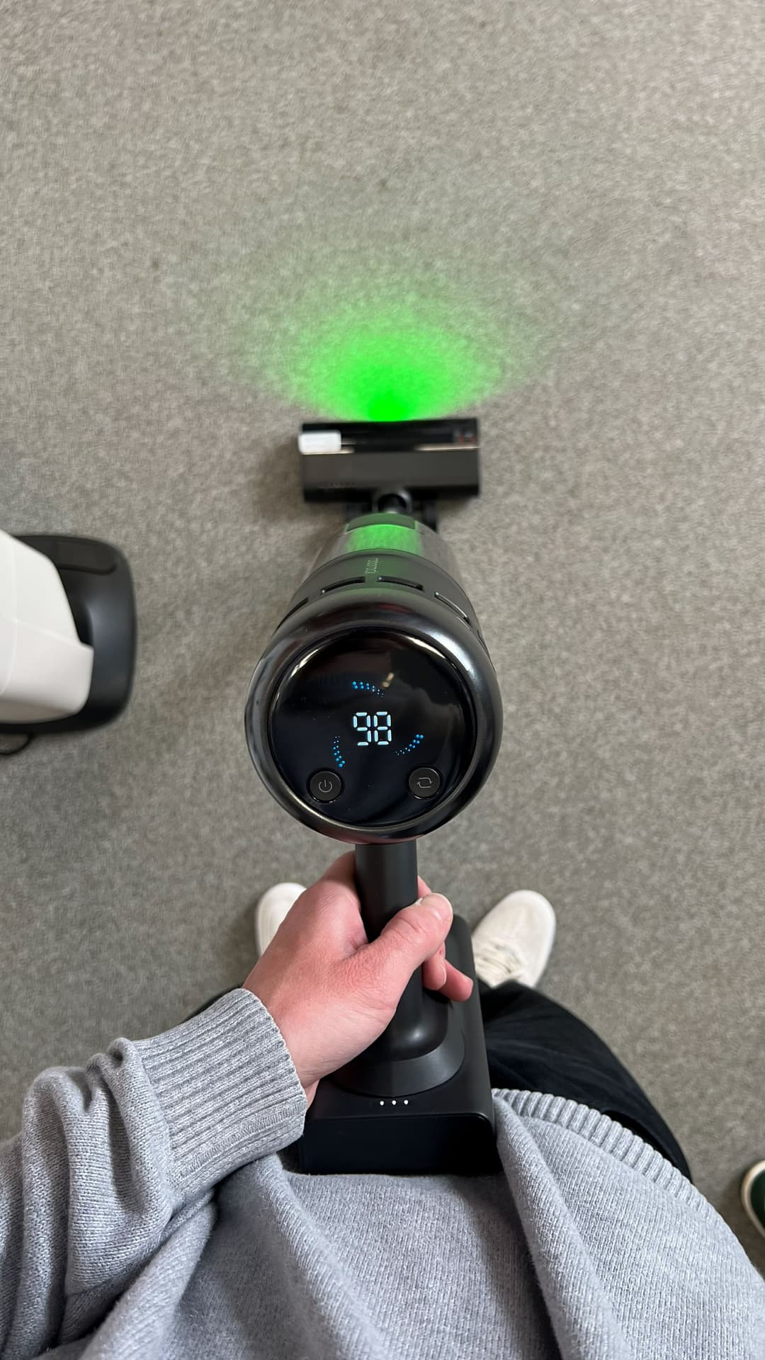 Tête du Roborock H60 Hub Ultra tenue en main, avec son écran digital affichant le mode de nettoyage et son faisceau LED vert orienté vers le sol