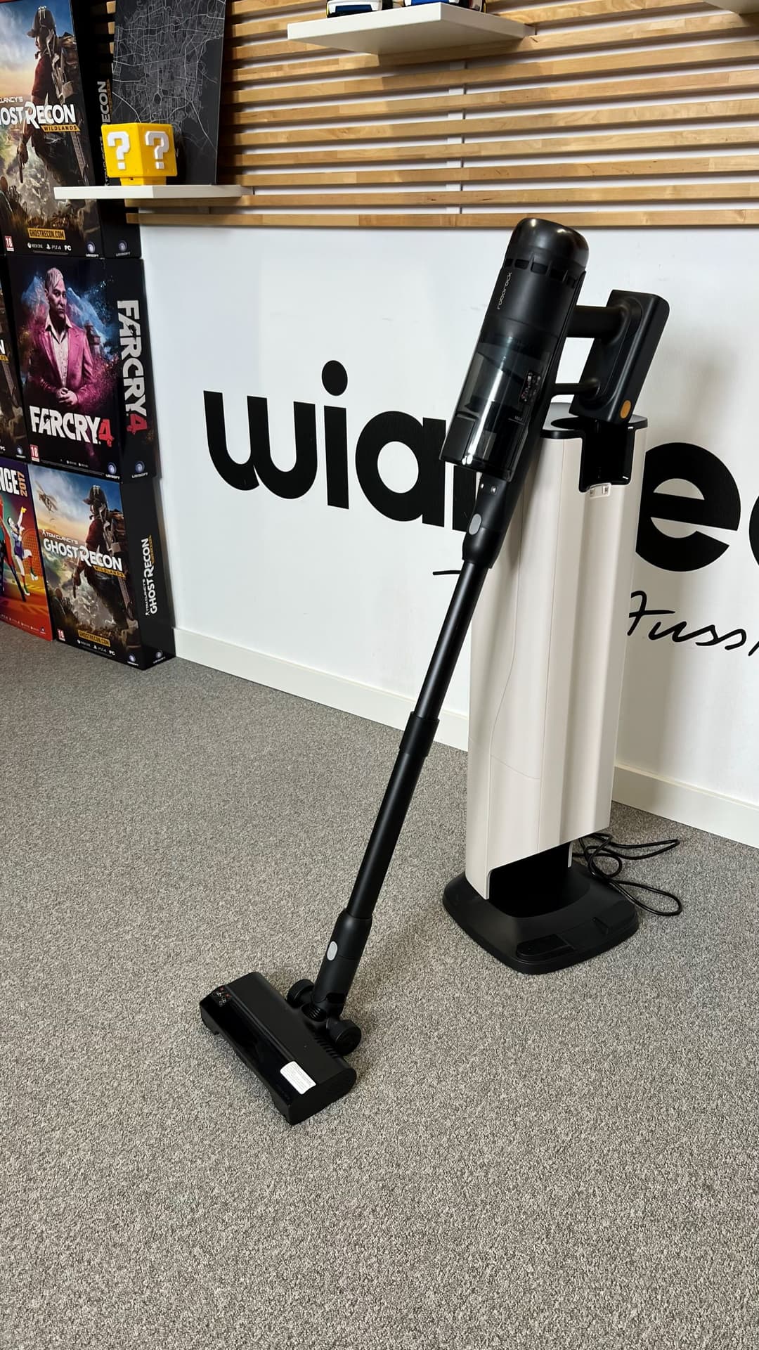 Roborock H60 Hub Ultra, aspirateur balai noir et blanc, posé sur le sol à côté de sa station de vidange automatique