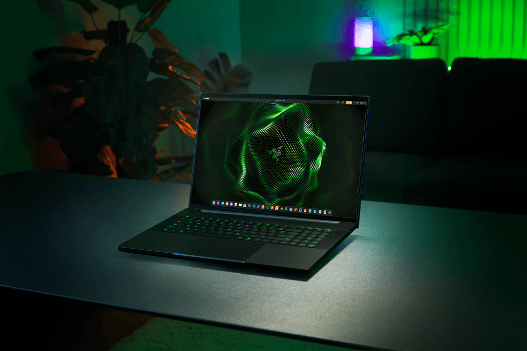 Razer Blade 18 noir ouvert affichant le logo Razer vert sur l'écran, clavier rétroéclairé vert, ambiance gaming avec éclairages RGB