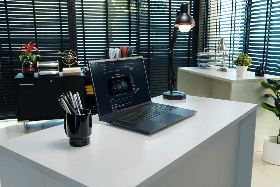 Razer Blade 18 posé sur un bureau blanc, affichant du code à l'écran, dans un bureau moderne avec stores bleus
