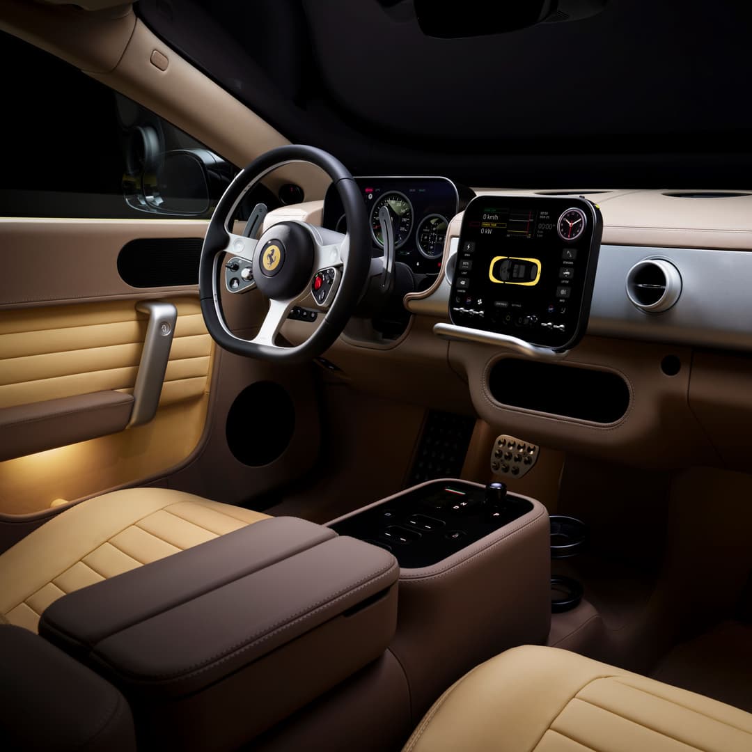 Habitacle de la Ferrari Luce avec volant noir et beige, écran tactile central affichant des données de batterie et d'autonomie en jaune, sièges beige et marron