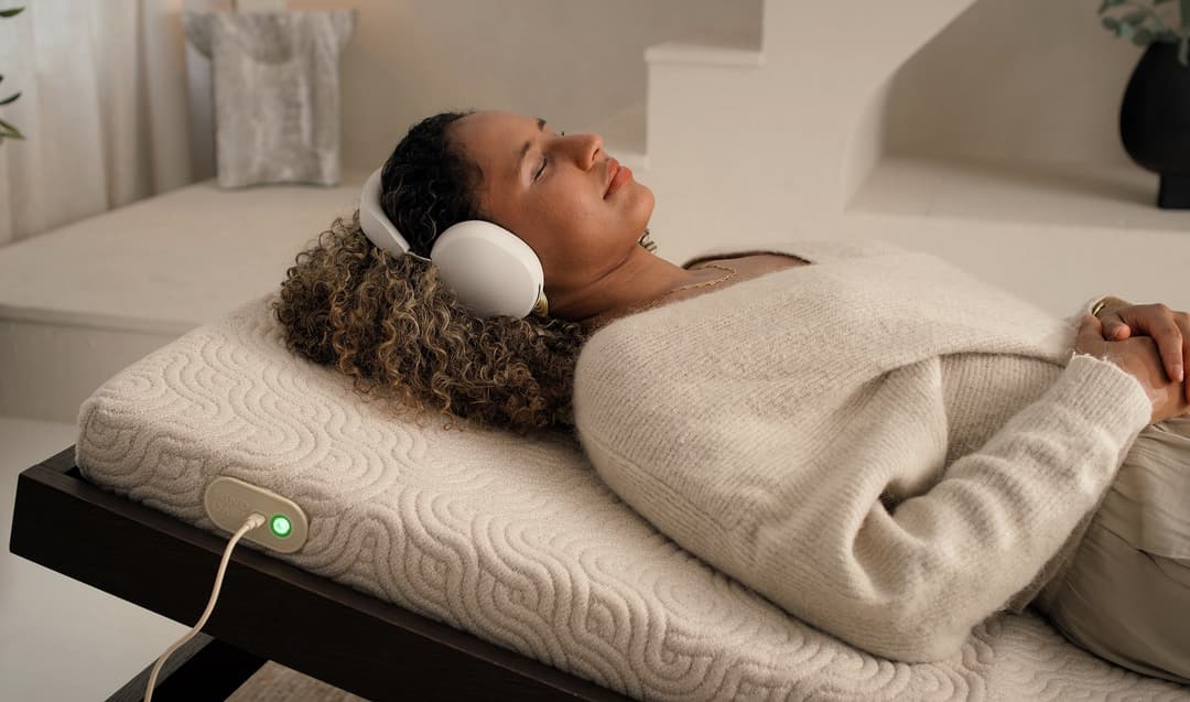 Personne allongée sur un coussin beige écoutant Mind Oasis At Home avec des écouteurs blancs