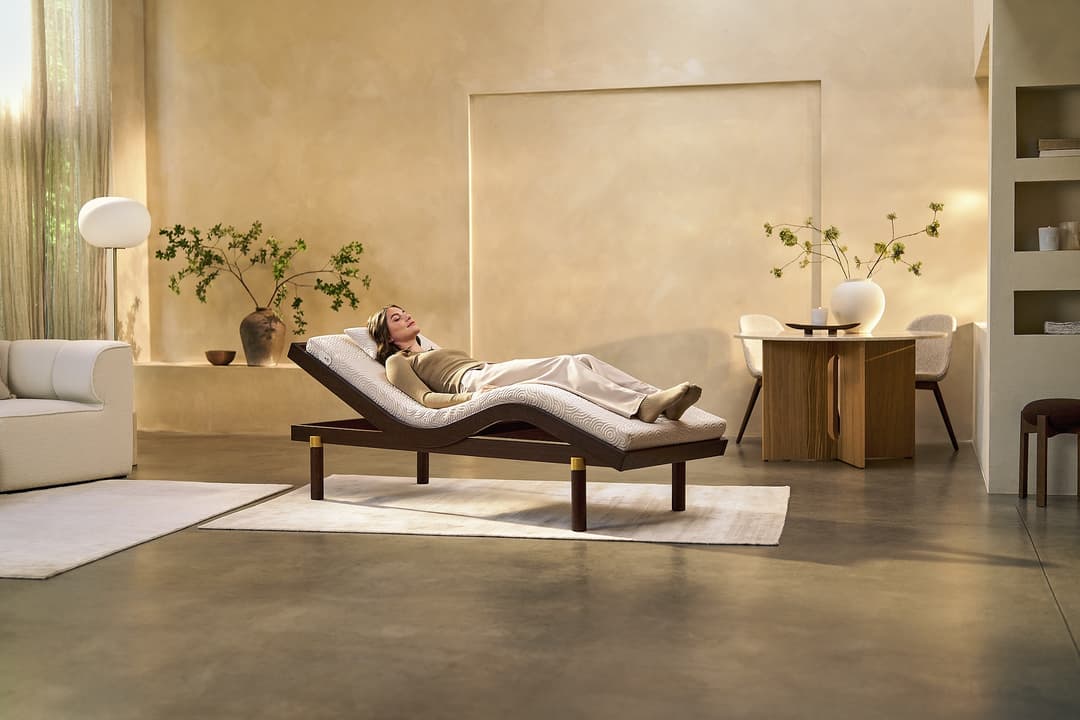 Femme allongée sur un lit ergonomique couleur crème dans un intérieur minimaliste aux tons beige et bois clair