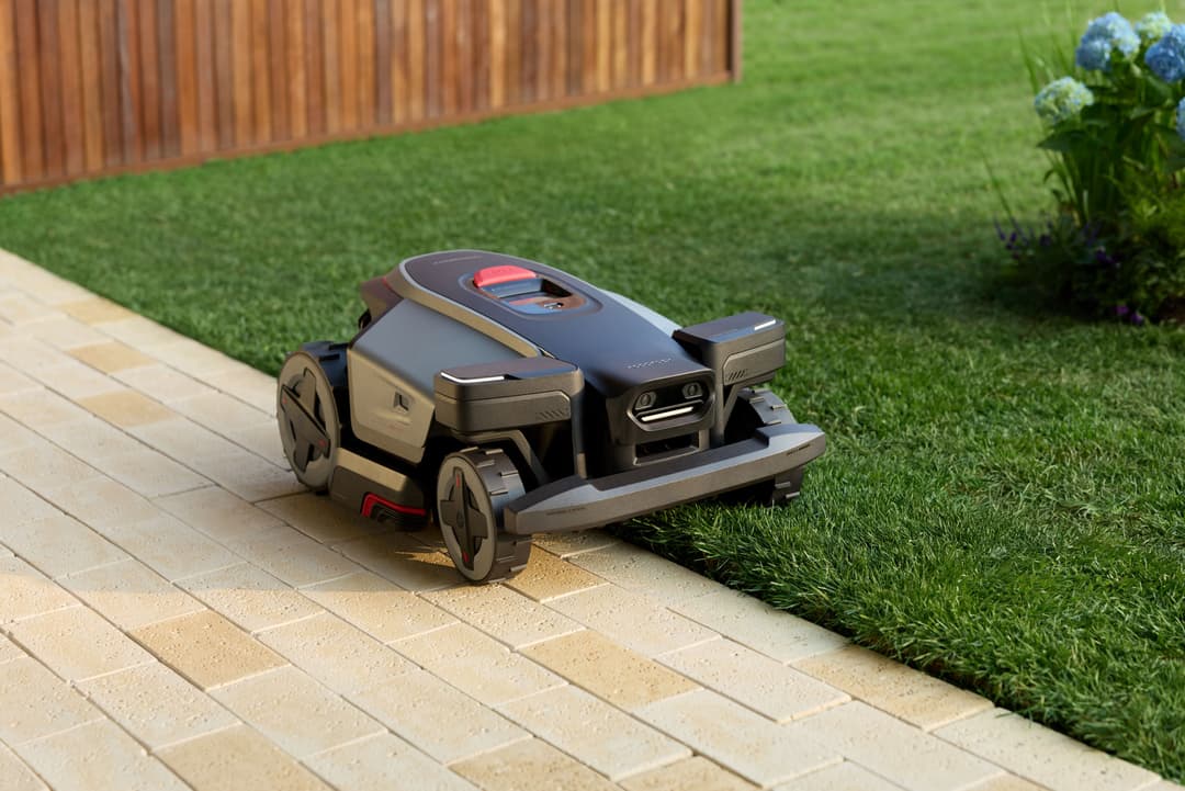 Robot tondeuse Roborock RockMow Z noir et gris sur une terrasse, près d'une pelouse verte avec clôture en bois