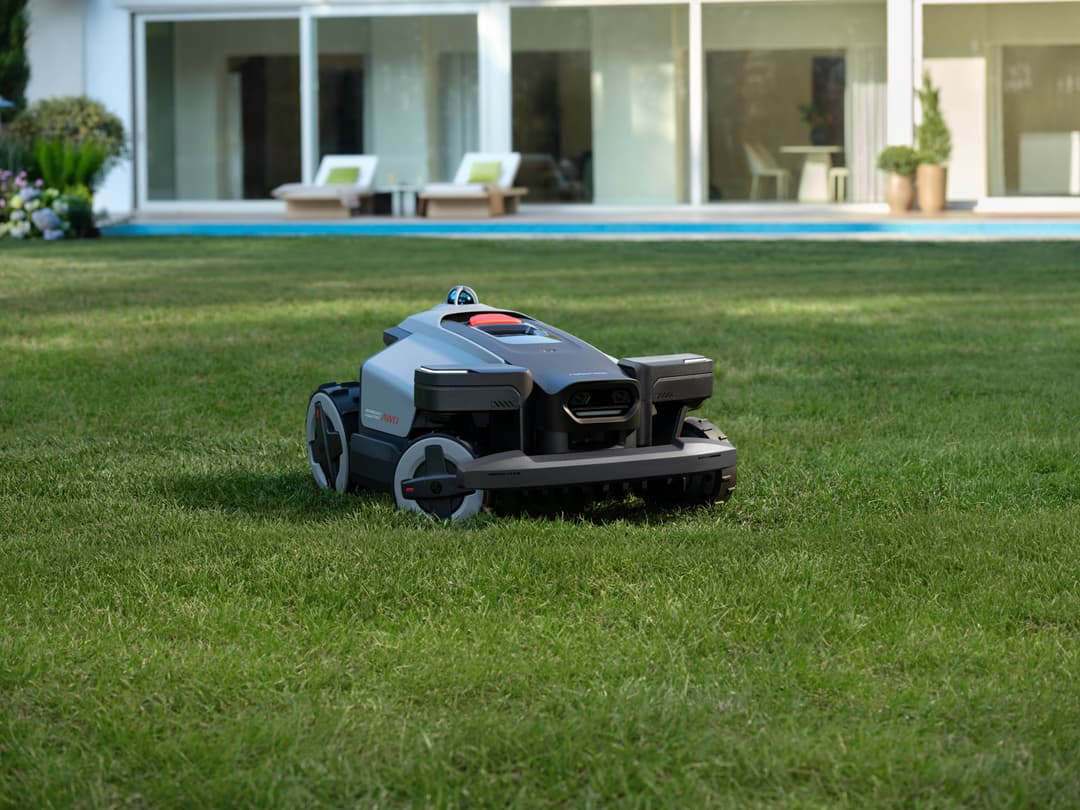Robot tondeuse Roborock blanc et noir en action sur un gazon vert devant une maison moderne avec piscine