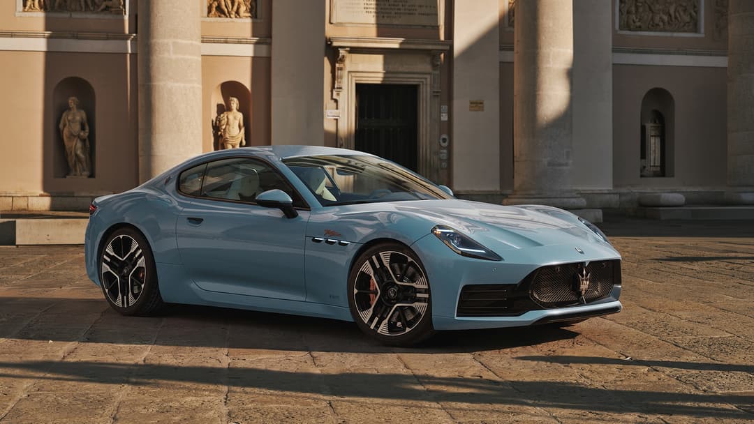 Maserati GranTurismo bleu ciel, coupé aux formes élancées, stationnée sur une piazza devant une façade classique