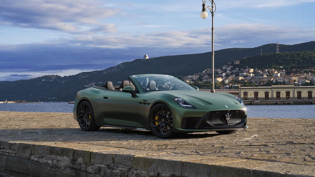 Maserati GranCabrio décapotable vert sapin garée au bord d'un lac avec montagnes et ville en arrière-plan