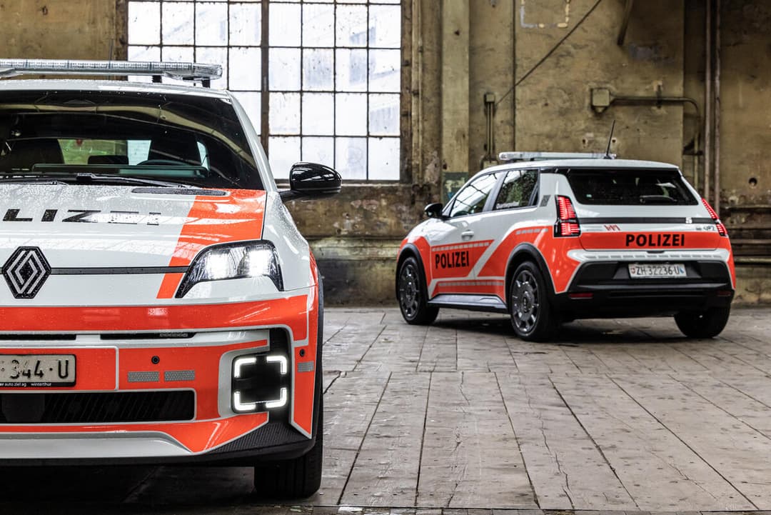 Deux voitures de police aux livrees rouge et blanc stationnees dans un garage : une Renault 5 E-Tech electric et un autre vehicule police