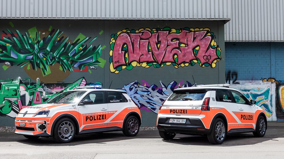 Deux Renault 5 E-Tech electric blanches et oranges aux marquages «POLIZEI», stationnées devant un mur de graffitis colorés