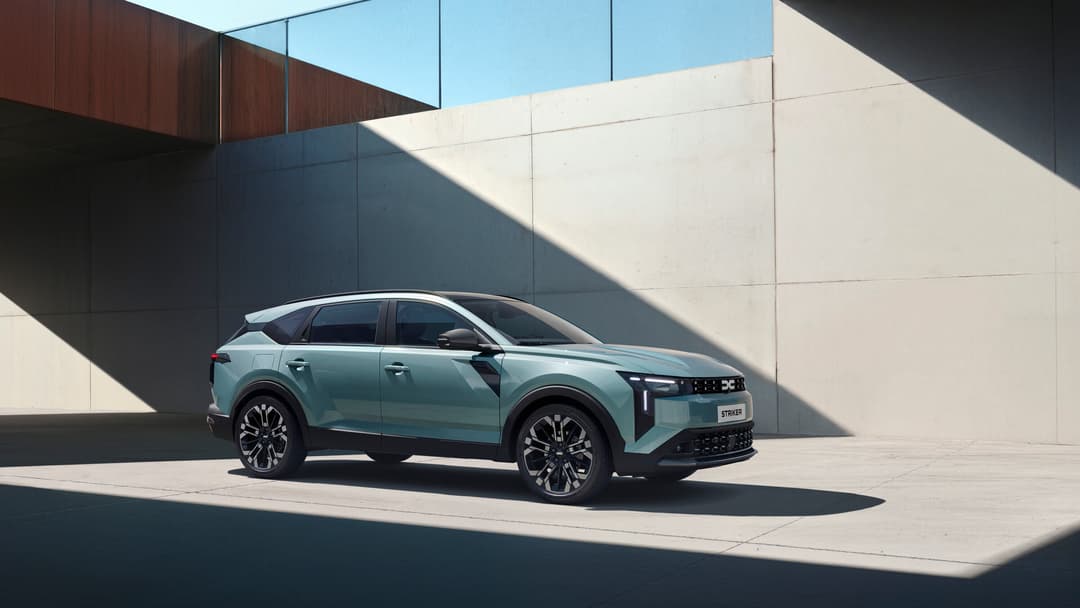 Dacia Striker de profil, SUV vert clair aux formes robustes et épurées, garé devant un mur gris moderne