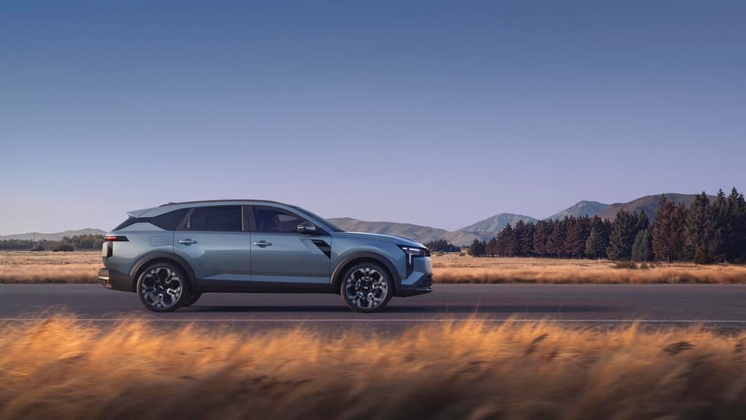 Dacia Striker bleu ciel en profil, stationné dans un paysage montagneux avec champs et forêts de conifères sous ciel dégagé
