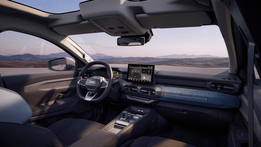 Habitacle du Dacia Striker avec volant, écran tactile, tableau de bord épuré et sièges beiges, vue sur paysage montagneux