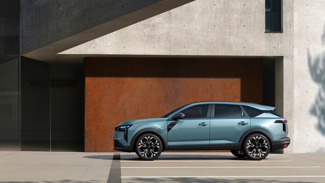 Dacia Striker bleu clair de profil devant un bâtiment moderne aux murs gris et orange rouille