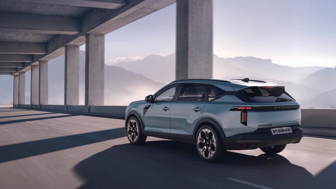 Dacia Striker blanc garé sous un viaduc, avec montagnes en arrière-plan
