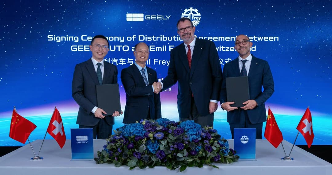 Cérémonie de signature entre Geely Auto et Emil Frey en Suisse, quatre hommes en costumes se serrant la main devant un fond bleu, drapeaux chinois et suisses