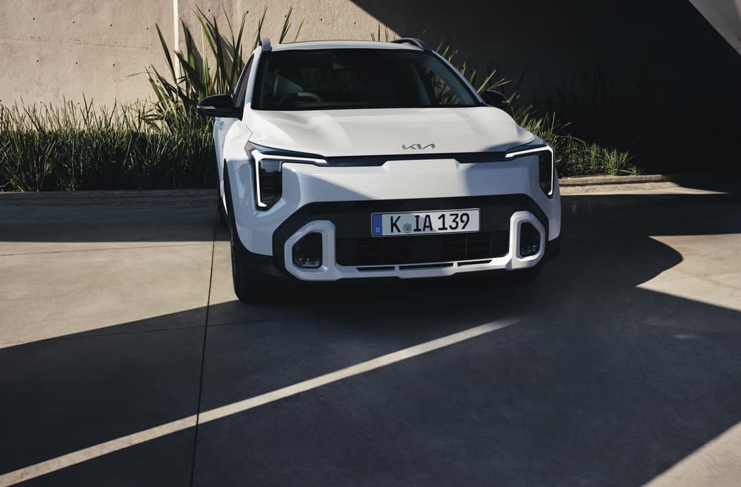 Kia Stonic Inspire blanc de face, stationné en plein soleil avec des plantes en arrière-plan