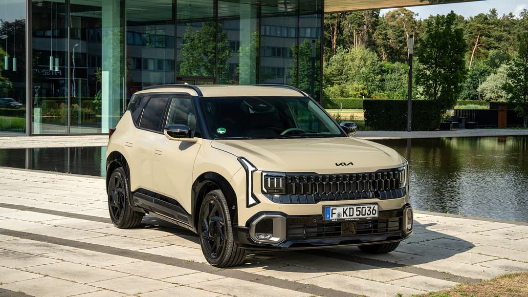 Kia Seltos blanc garé au bord de l'eau, avec design moderne et calandre distinctive, devant un bâtiment aux façades vertes