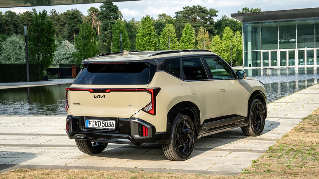 Kia Seltos beige de profil, stationnée au bord d'un lac, devant bâtiment moderne et arbres verts