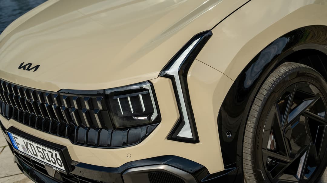 Kia Seltos beige clair, détail de la face avant avec calandre noire, phares LED et logo Kia