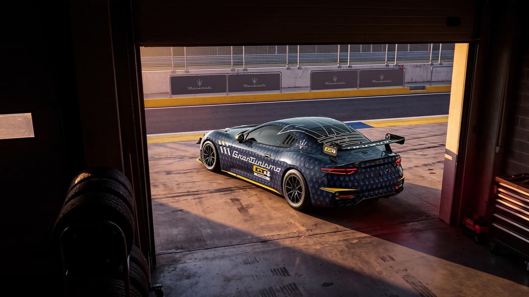 Maserati Project GT4 noir avec motifs bleus exposée sur un circuit automobile, vue de trois-quarts arrière