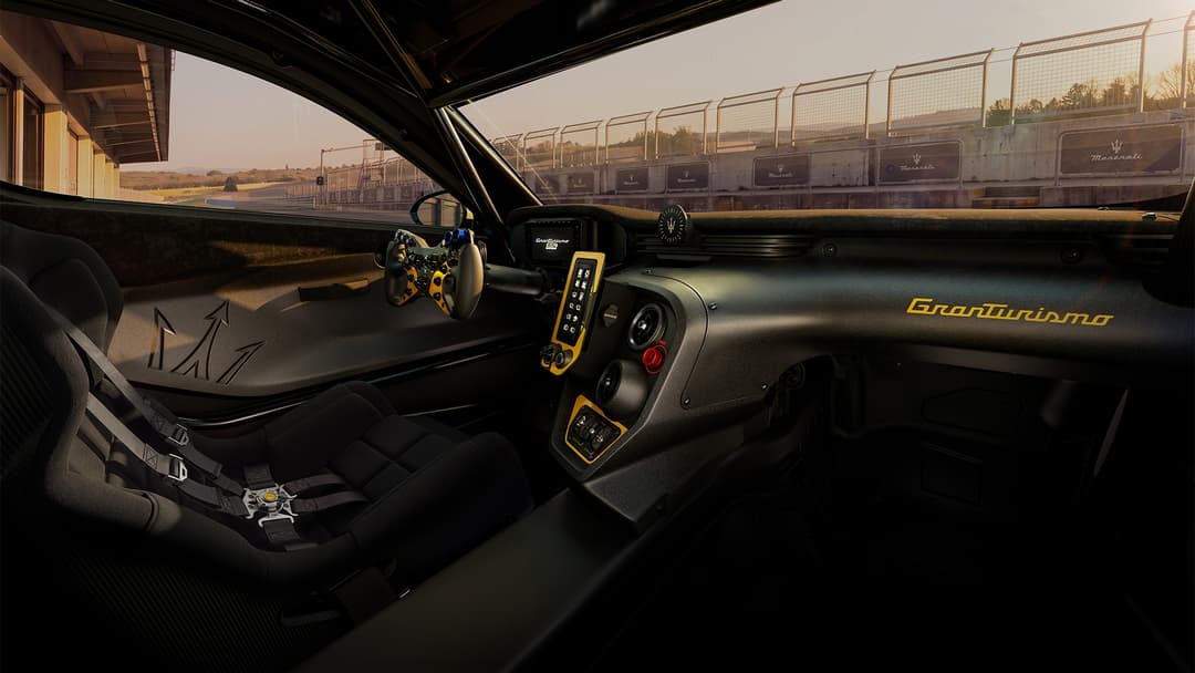 Habitacle du Maserati Project GT4 avec siège baquet, volant de course doré, tableau de bord noir aux accents jaunes et arceau de sécurité, circuit en arrière-plan