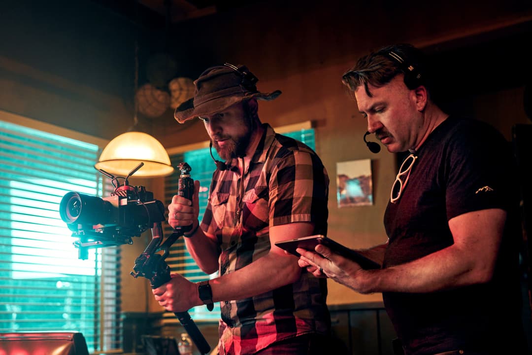 Deux cinéastes manipulent une caméra Sony FX5 sur cage, l'un contrôlant à distance via une tablette, dans un studio aux lumières turquoise et orangée