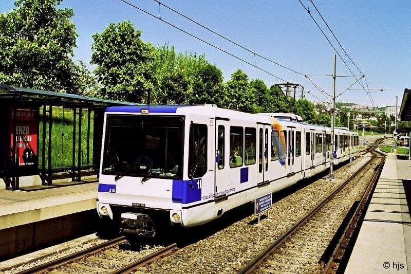 Tram blanc et bleu du réseau TL de Lausanne arrêté en gare sous un ciel ensoleillé