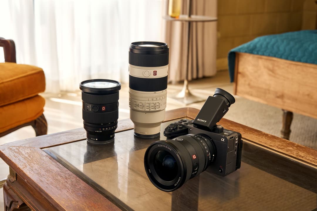 Caméra Sony FX5 noire avec viseur amovible, entourée de deux objectifs et posée sur une table en bois dans un intérieur élégant