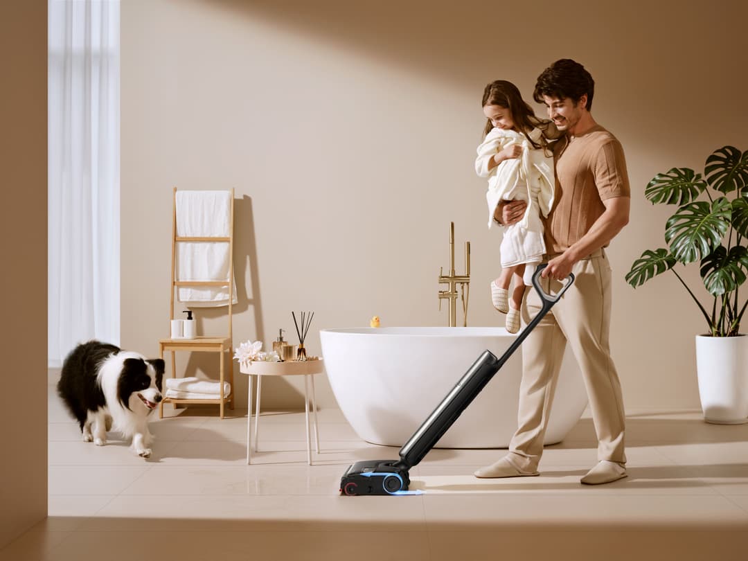 Dreame T16 Pro Heat nettoyant le sol d'une salle de bain, manié par un homme tenant un enfant, près d'un chien et d'une baignoire