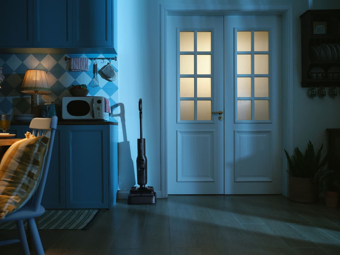 Roborock F25 Steam positionné au centre d'une cuisine bleue moderne, nettoyant le sol devant des portes vitrées