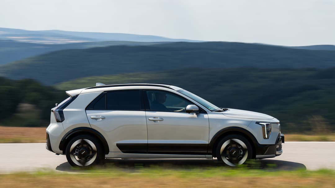 Kia Niro blanc en profil roulant sur route, montagnes en arrière-plan, design modernisé avec nouvelle signature lumineuse