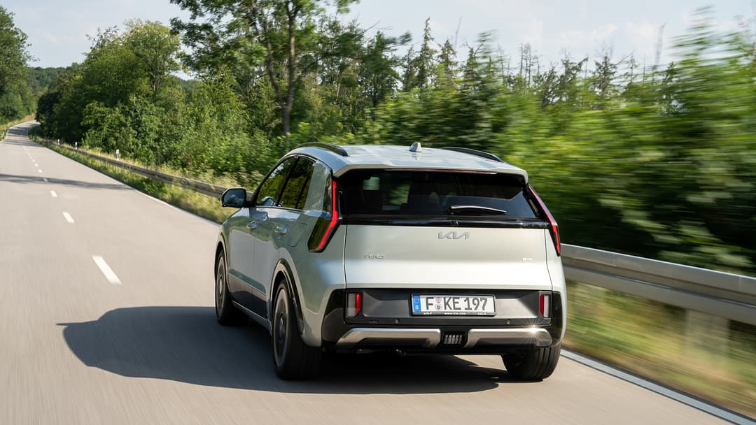 Kia Niro blanc circulant sur une autoroute entourée de forêt, vue de trois quarts arrière
