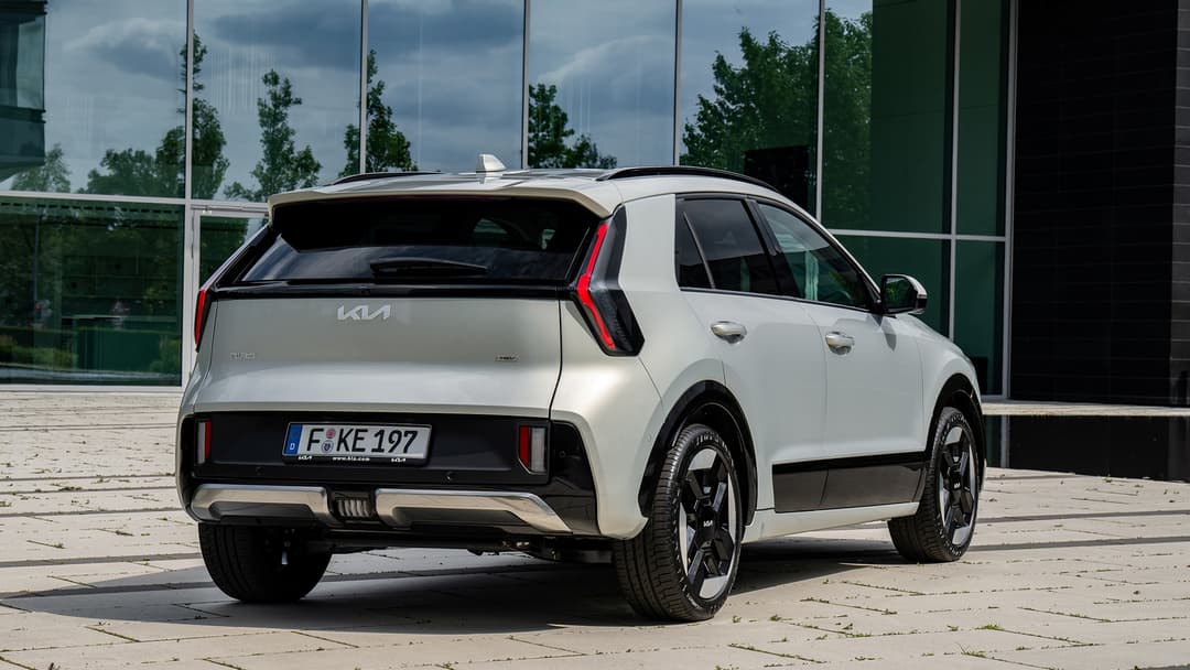 Kia Niro blanc hybride de trois-quarts arrière, stationnné devant un bâtiment moderne aux vitres vertes