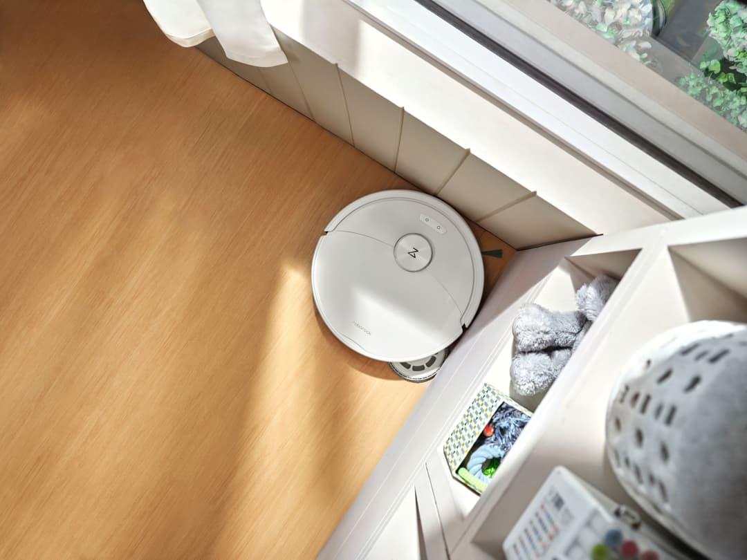 Robot aspirateur Roborock Qrevo 2 ProX blanc circulaire sur parquet, près d'une station de nettoyage blanche