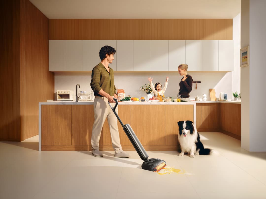 Homme utilisant un nettoyeur Dreame T Series ultrafin dans une cuisine moderne avec deux femmes et un enfant, un chien assis à proximité