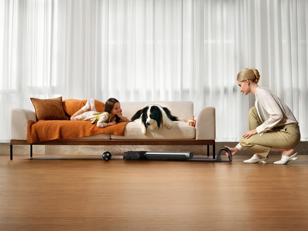 Femme utilisant un aspirateur robot Dreame T Series dans un salon, tandis qu'une enfant et un chien jouent sur un canapé beige