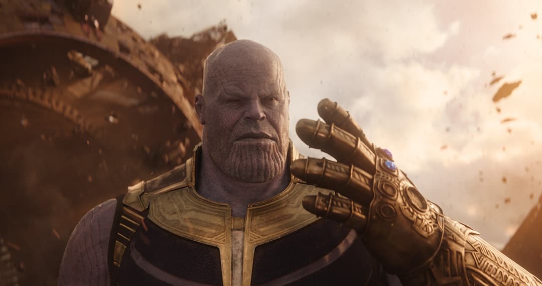 Thanos, géant violet à la barbe noire, portant une armure dorée et noire, le poing levé dans un décor de ruines et de ciel teinté d'orange