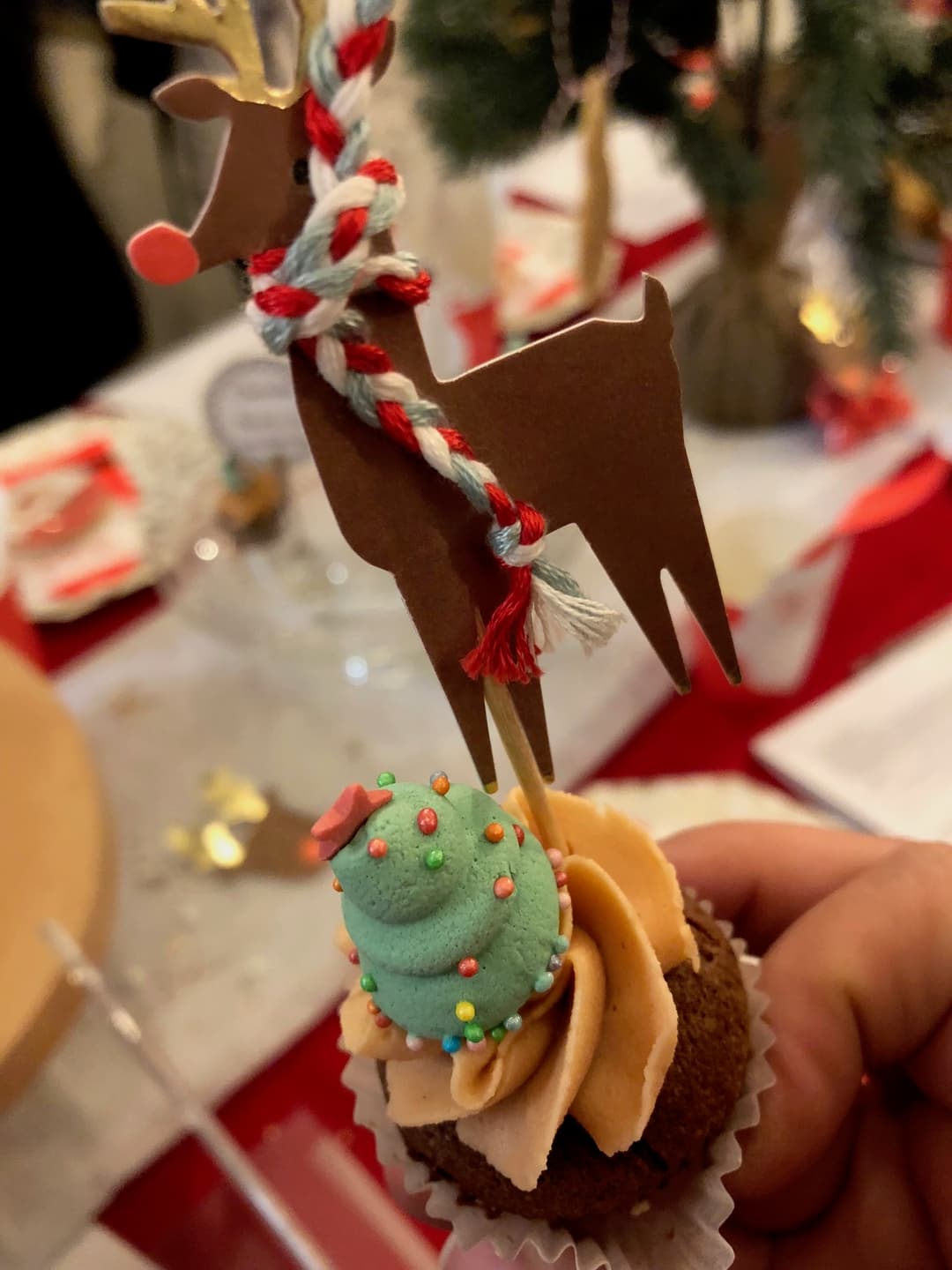 Cupcake au chocolat garni de crème verte décorée de perles colorées, surmonté d'une silhouette de renne en chocolat avec un collier rouge et blanc