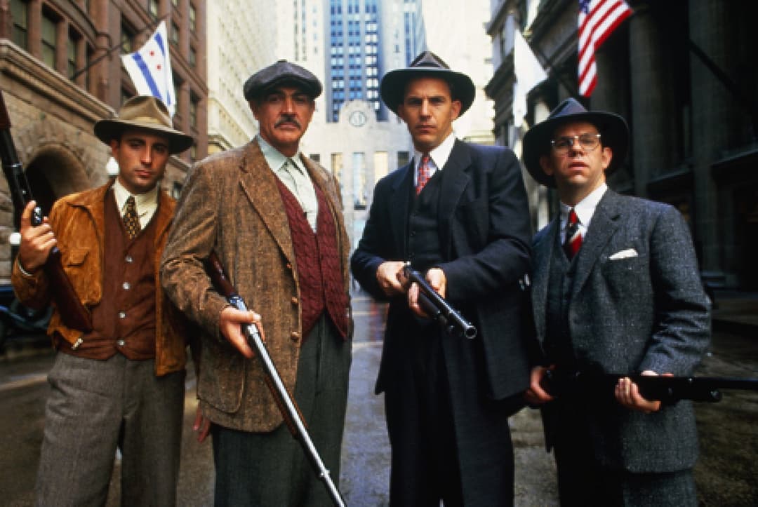 Quatre agents fédéraux en costume années 1930 posent dans une rue de Chicago avec des armes, drapeaux américains en arrière-plan