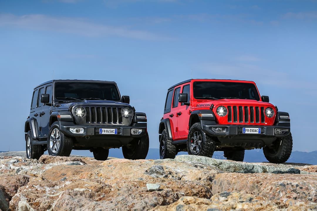 Deux Jeep Wrangler, l'une bleu foncé et l'autre rouge, stationnées côte à côte sur un terrain rocheux avec ciel bleu en arrière-plan