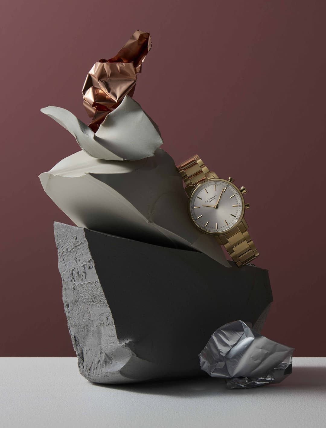 Montre Kronaby Sweden à bracelet doré posée sur une composition abstraite de formes géométriques et matériaux contrastés