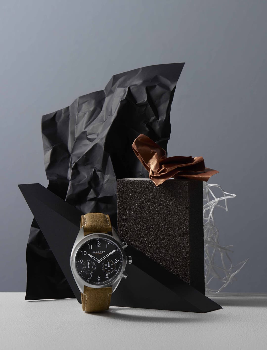 Montre Kronaby Sweden au boîtier argenté et bracelet olive devant son emballage noir et sa boîte