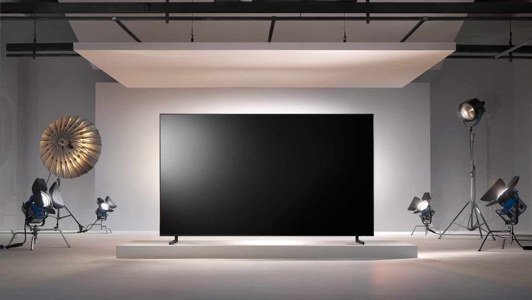 Téléviseur Samsung QLED 8K noir sur piédestal blanc dans un studio de présentation avec projecteurs