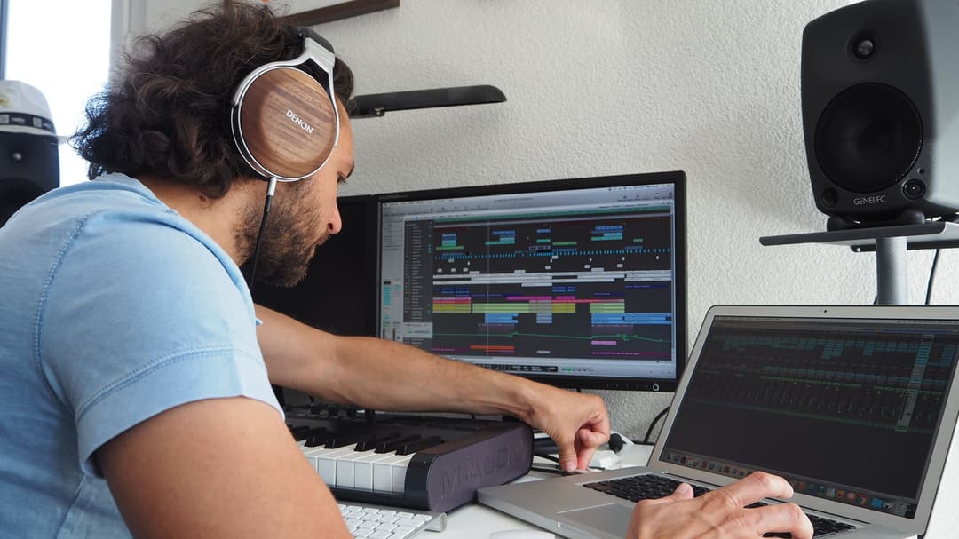 DJ Gil Everest portant le casque Denon AH-D7200 marron et blanc, travaillant sur sa station de production musicale avec écrans et contrôleur