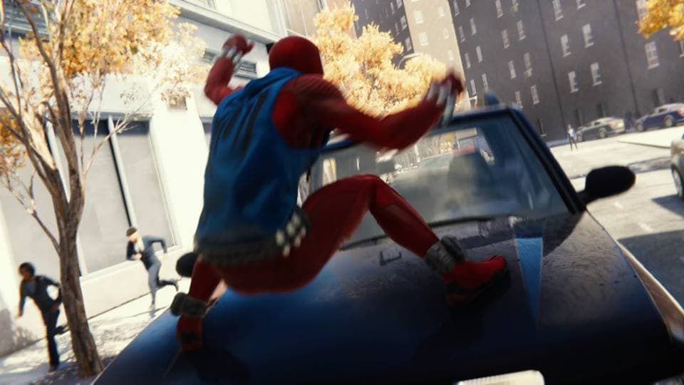 Spider-Man en costume rouge et bleu saute sur un véhicule dans une rue de ville, les bras levés