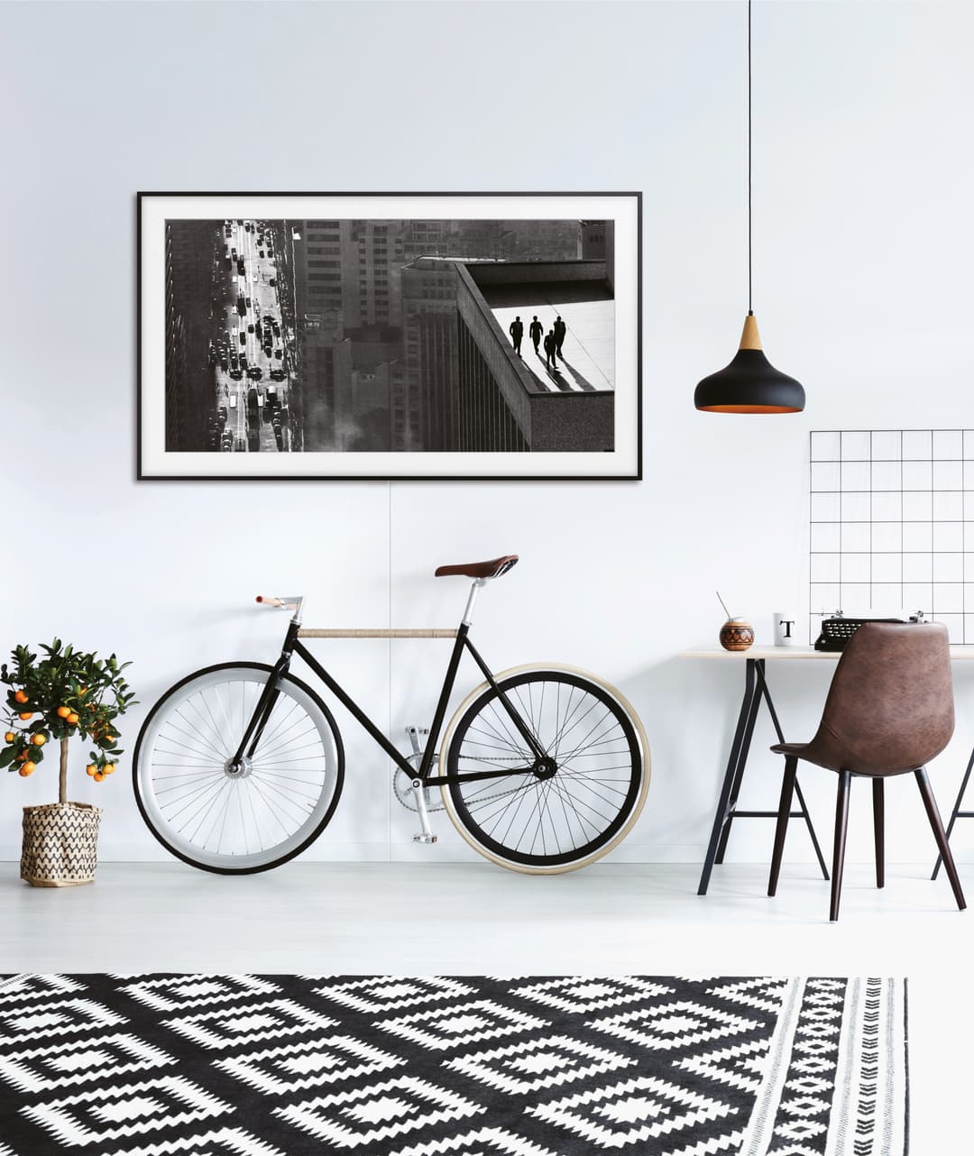 Samsung The Frame 2.0 avec cadre noir affichant une photo en noir et blanc, suspendu au-dessus d'un vélo et d'un bureau dans un intérieur moderne