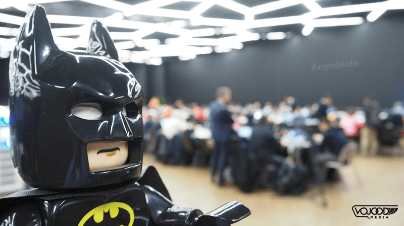 Figurine Batman noir en gros plan au Salon International de l'Automobile de Genève, avec visiteurs floutés en arrière-plan